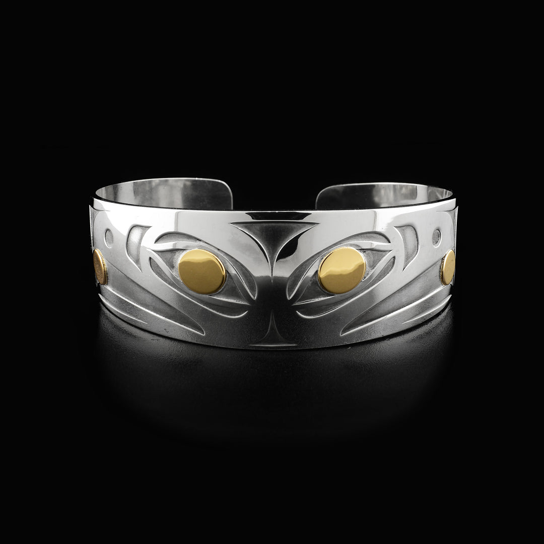 Side-view of two raven heads, back-to-back. Laser-carved with oxidized silver background. Both ravens have a 14K gold ball in their beak and 14K gold in their visible eye. Minimalist design, by Tahltan artist Grant Pauls. Bracelet is sterling silver.