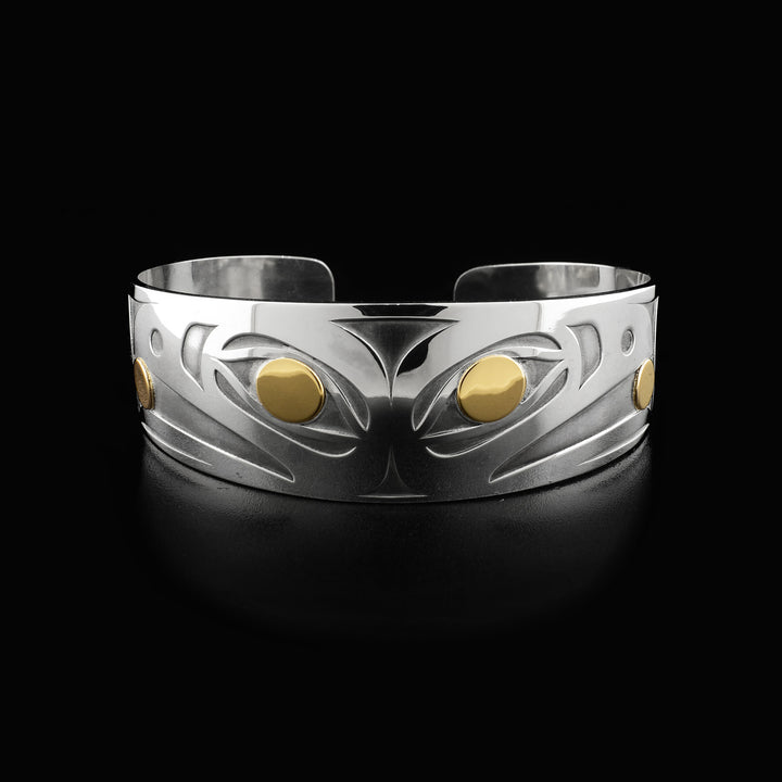 Side-view of two raven heads, back-to-back. Laser-carved with oxidized silver background. Both ravens have a 14K gold ball in their beak and 14K gold in their visible eye. Minimalist design, by Tahltan artist Grant Pauls. Bracelet is sterling silver.