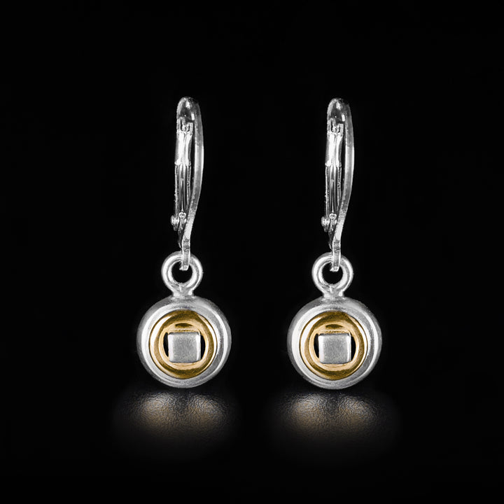 These drop circle in circle earrings are made form sterling silver and 14K gold. The hangs are small, circular and have gold, ring highlights in them. There is a silver square held in the center cutout.