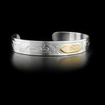 Depicts 14K yellow gold sun with rays on front. Rest of piece is sterling silver and right side with carved raven is also visible. By Kwakwaka’wakw artist Victoria Harper.