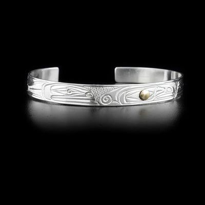 Bracelet features two orcas facing thunderbird head in the middle. Side-view of thunderbird head with gold in the eye. By Heiltsuk artist Reg Gladstone.