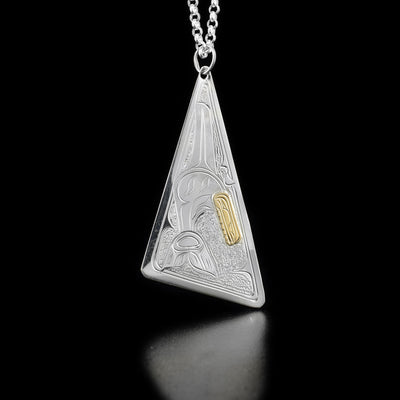 Sterling silver upwards-pointing triangle pendant featuring swimming orca with 14K yellow gold head. Textured background.
