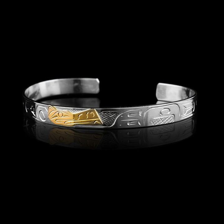Wolf Cuff Bracelet features a hand-carved sterling silver band adorned with traditional Indigenous markings. At its center, the Wolf Legend is meticulously engraved into 10K gold, creating a beautiful contrast between the metals.