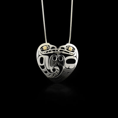 Side-view of sterling silver wolf and eagle facing each other, their shapes form a heart. Their features are laser-cut, leaving pierced out spaces. 18K yellow gold in both the visible eyes.