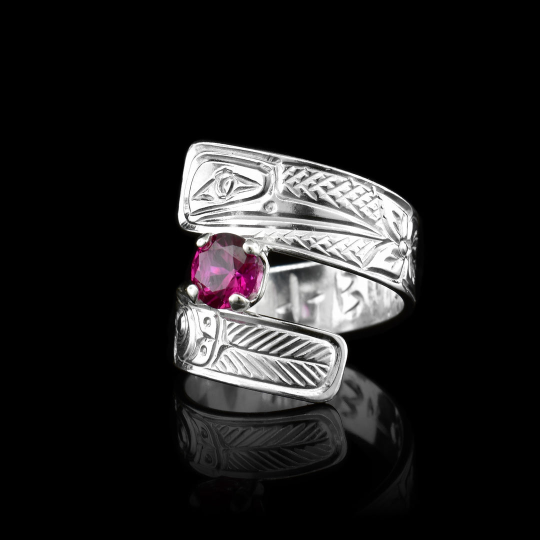 This red gemstone ring is made from sterling silver and has a wrapped, tapered band. There is a depiction of a flower and the Hummingbird carved into the surface of it.