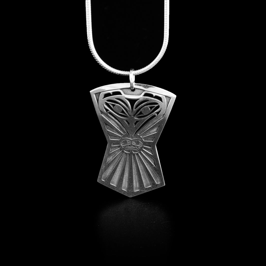 This raven and sun pendant holds the shape of a shield. The head of the raven facing forward is at the top with a small sun in its beak.