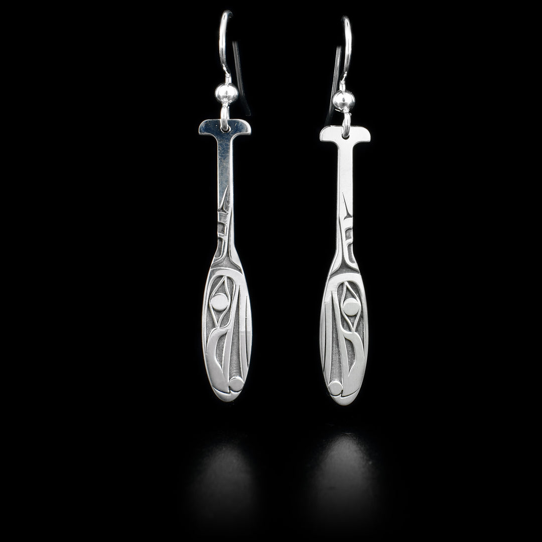 These sterling silver dangle earrings have hangs that are shaped like paddles. There are depictions of the Raven carved into the surface of them.