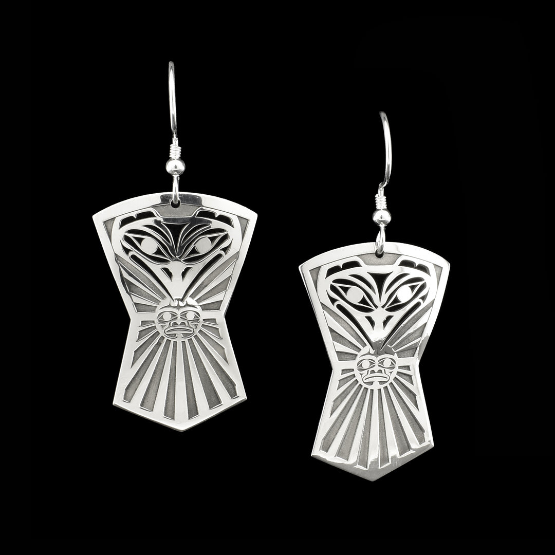Sterling silver pierced dangle earrings. Both earrings in shape of Indigenous shield and depict front view of raven’s head with sun in beak.