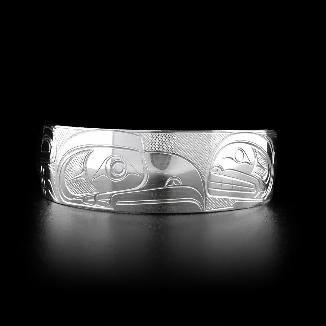 This Orca and Eagle bracelet is made from sterling silver and has a wide, tapered band with a gap in the back. There are depictions of the Eagle and the Orca carved into the surface of the band.