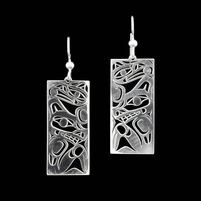 Rectangular earrings with pieces cut out to create design. Raven with ball in beak above wolf. Wolf below with paw up and curled over.