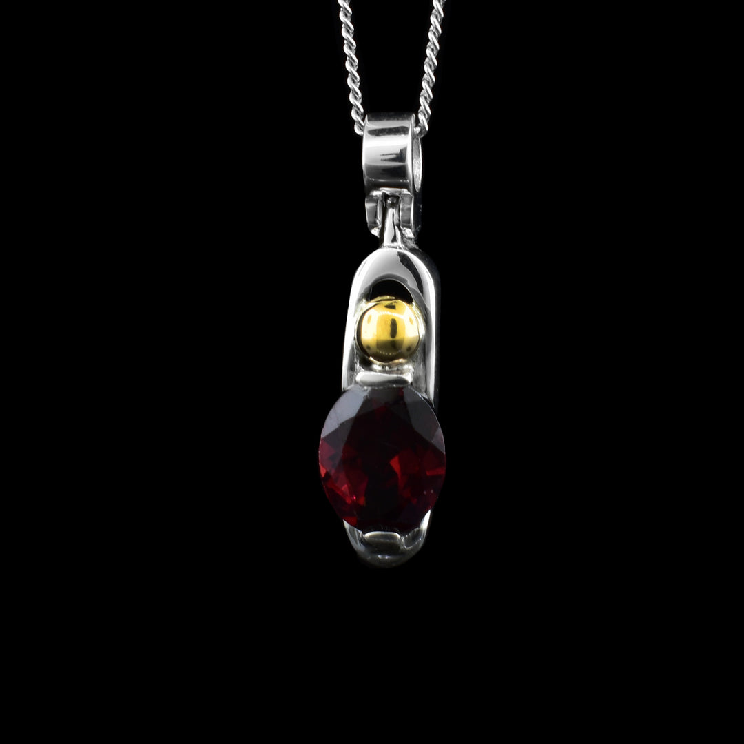 Silver and Gold Garnet Pendant. A red oval garnet is casted inside a piece of sterling silver with a secure 14k gold sphere a top.
