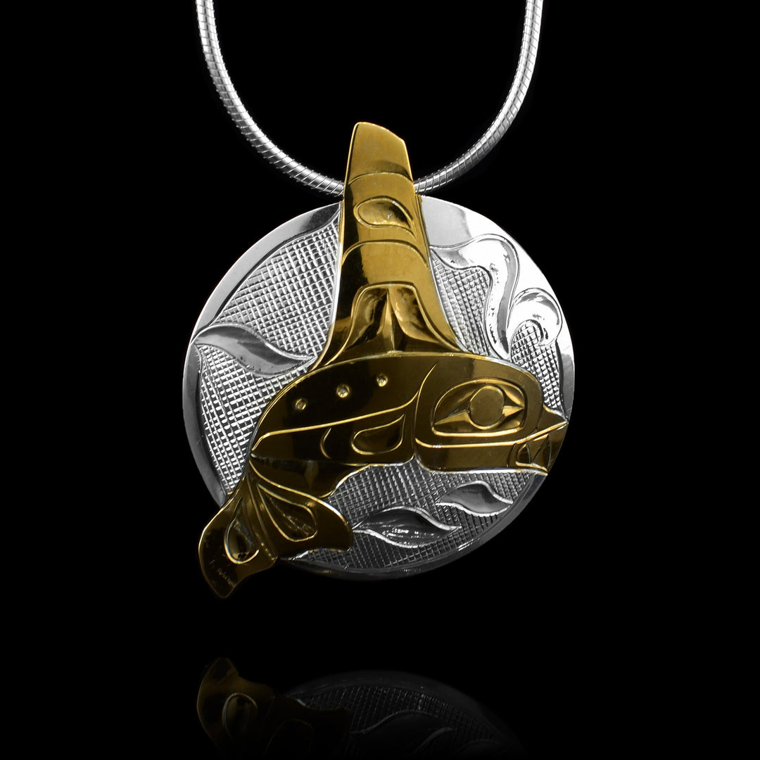 This circular sterling silver circular pendant has been hand carved with the look of the ocean. In the middle of the silver circle is a gold orca. 