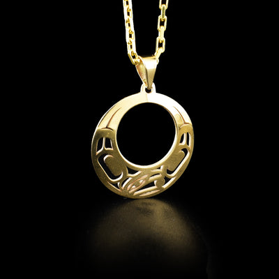 Round yellow gold cut-out pendant with pierced raven design. Raven’s head on bottom, facing left, with ball in beak. Designs on either side of the head depict wings. By Tahltan artist Grant Pauls.