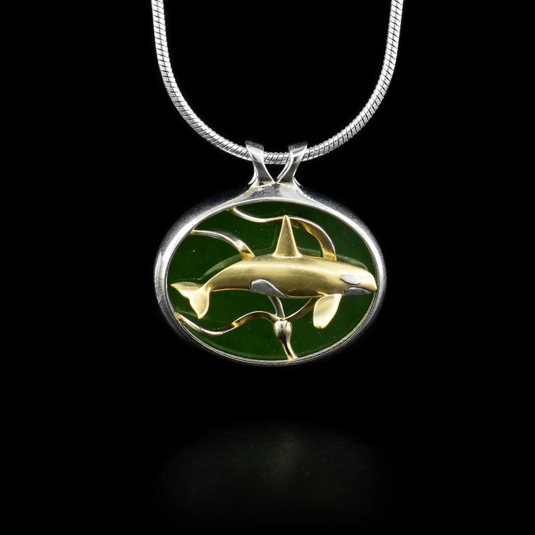 Pendant features gold and silver whale swimming among gold kelp. Background is A+ grade BC jade. Framed in sterling silver. By Dennis Kangasniemi.