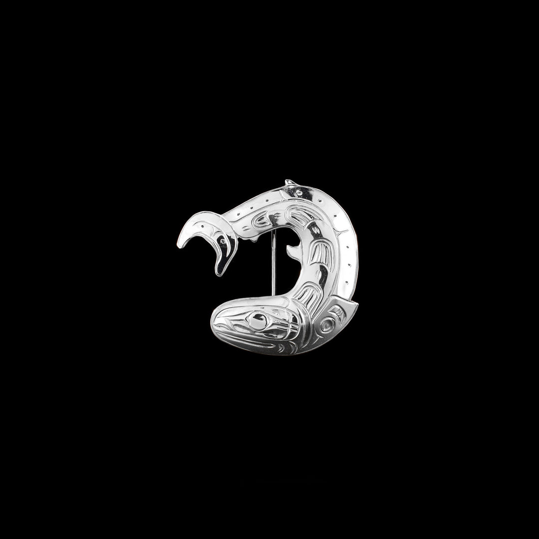 Salmon swimming in a circle. Design is made up of ovoids and lines. Salmon has been cut out of silver, giving edges an almost graphic look. Made of sterling silver.