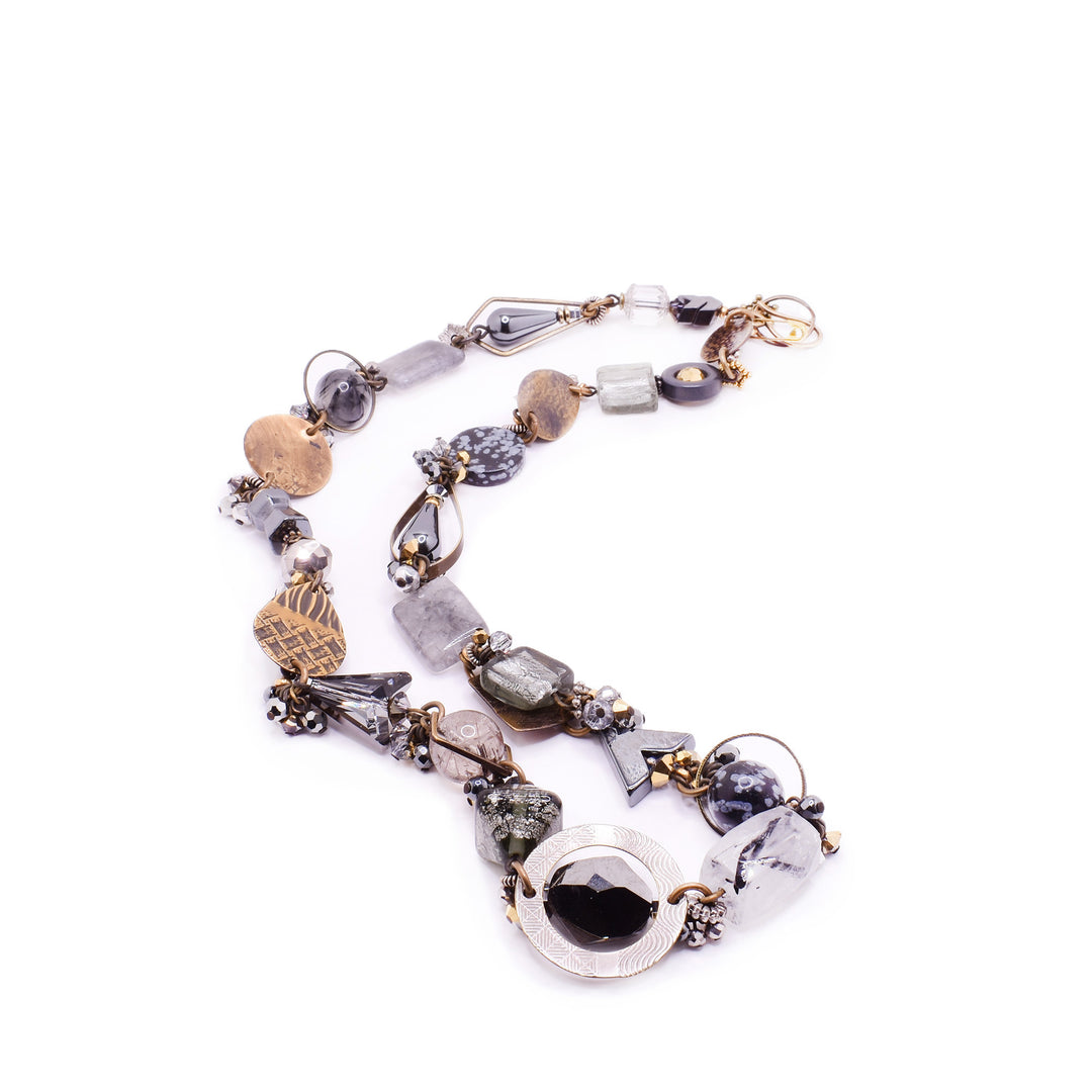 This beaded necklace features many different white, grey, black, and clear gemstones to represent the foggy mornings of fall. There are rich brown brass accents throughout the piece as well as the clasp at the back.