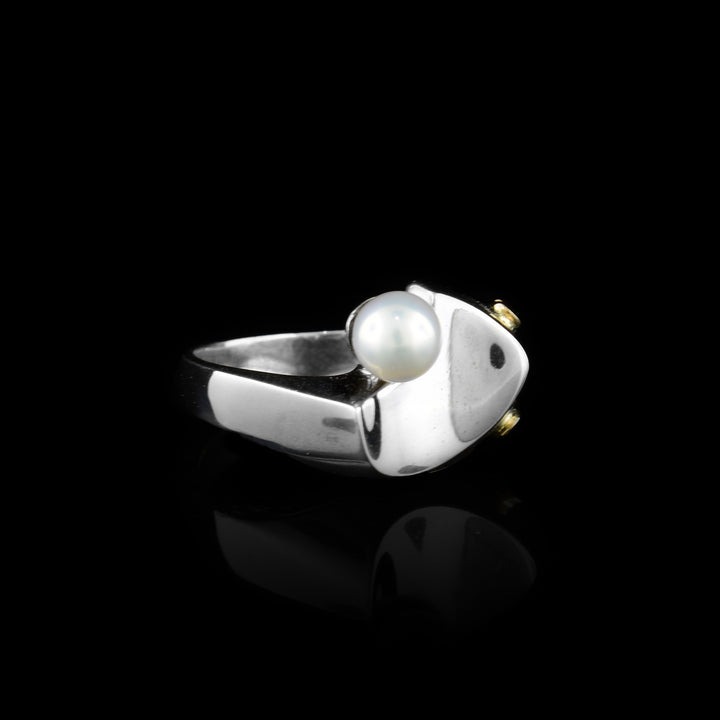 This gold pearl ring is made from sterling silver, 14K gold and freshwater pearl. The silver band is thin and there is a pearl at the top of it; there are gold highlights running around the pearl.