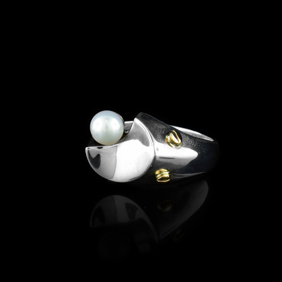 This gold pearl ring is made from sterling silver, 14K gold and freshwater pearl. The silver band is thin and there is a pearl at the top of it; there are gold highlights running around the pearl.