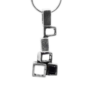 This abstract pewter pendant is made up of several, cutout and pewter squares. The squares are stacked at different angles and drop down before making a small cluster at the bottom. There is black glass in the center of the most bottom square.