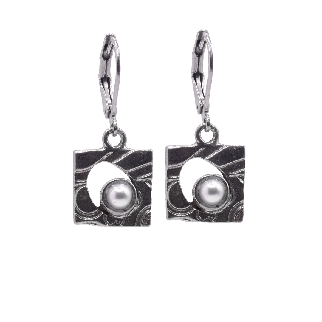 These dangling square earrings have hangs made from pewter with wavy designs on the surface of them. There is a cutout in the middle of the hangs with a round, Swarovski pearl in them.