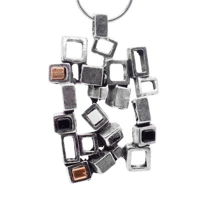 This pewter pendant is roughly square shaped and is made of many cutout, pewter squares that are attached together at different angles. There are gold plated and black glass pieces that are in the center of some of the squares.