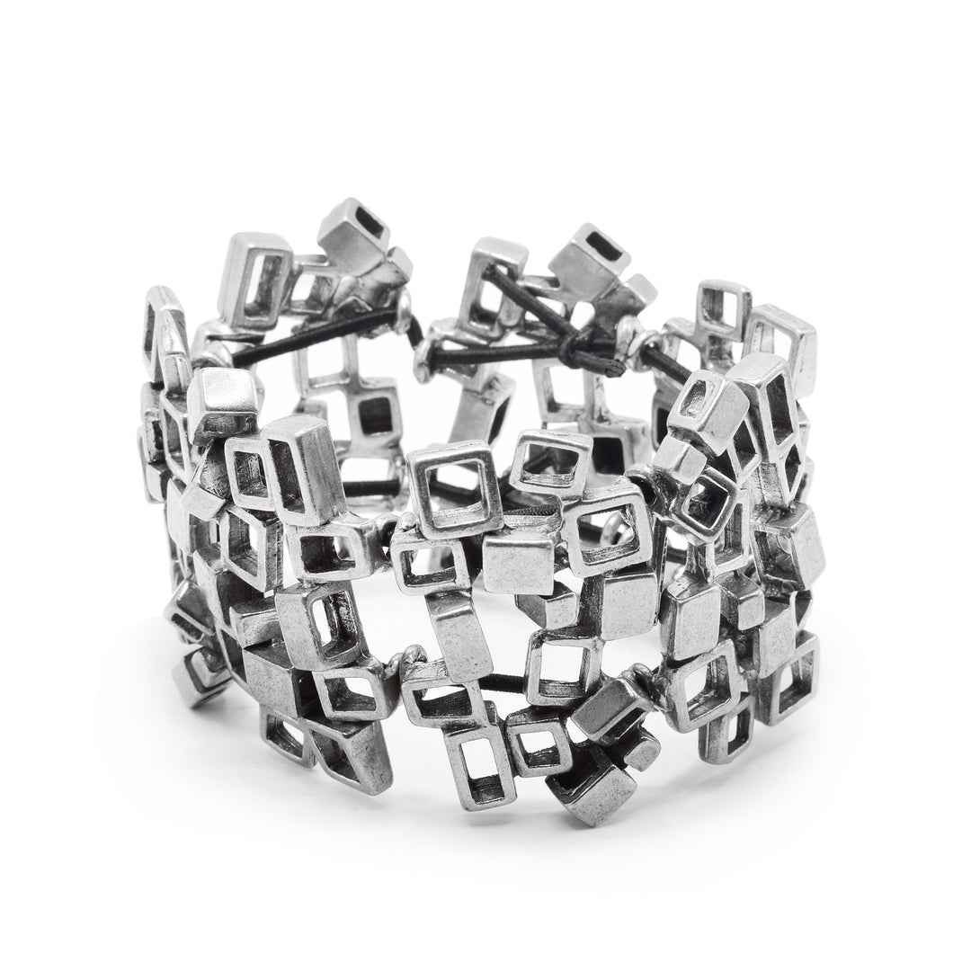 This pewter cuff bracelet is made using a combination of small, pewter cubes that have their middles cutout. The cubes are attached together to form this bangle with a solid, all around band. The band is wide and have a rugged texture due to the angles of the cubes.
