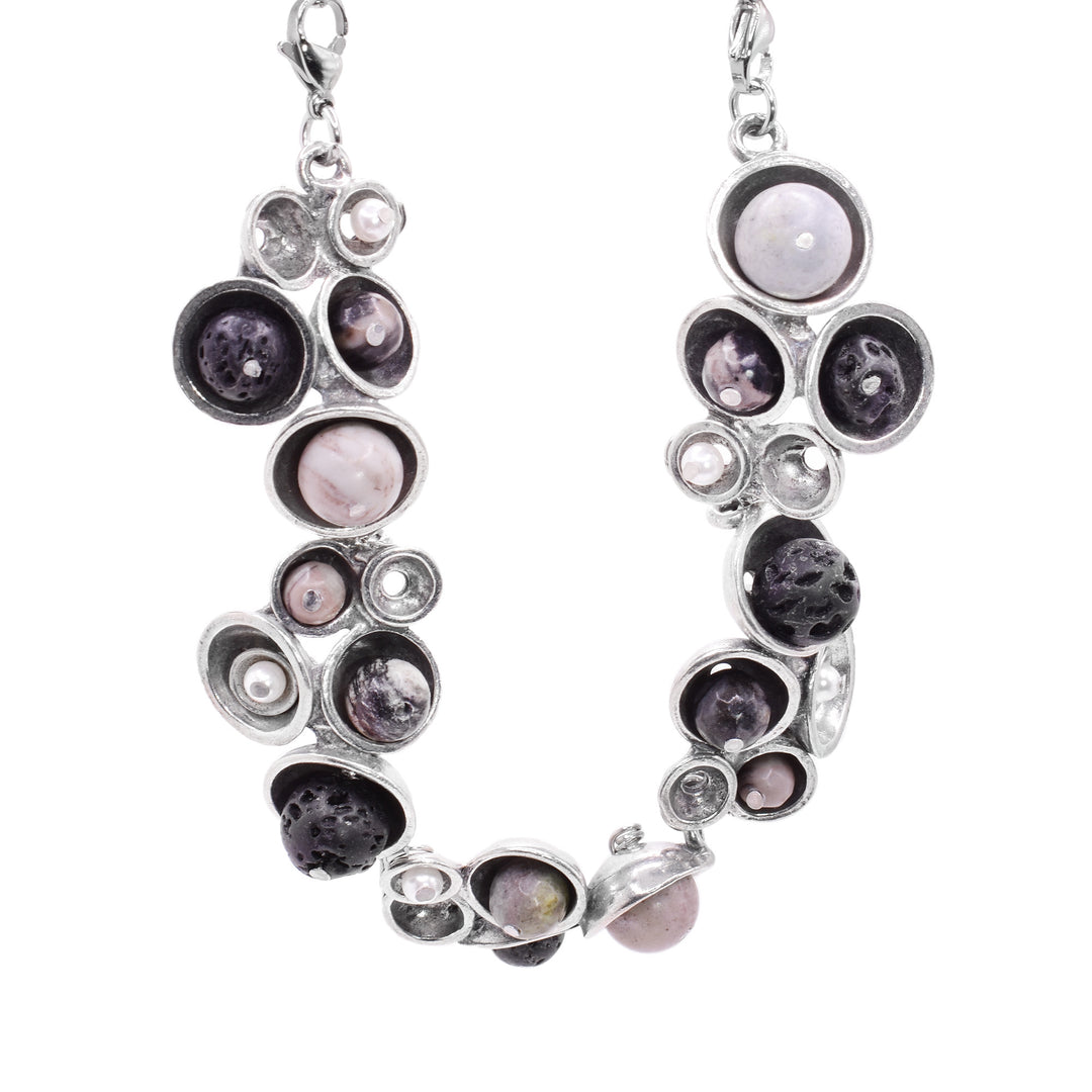 This pewter pendant has pewter, hollow half circles of different sizes with freshwater pearls and black, lava rocks held in them. The pearls and rocks are only on the bottom half f the necklace.