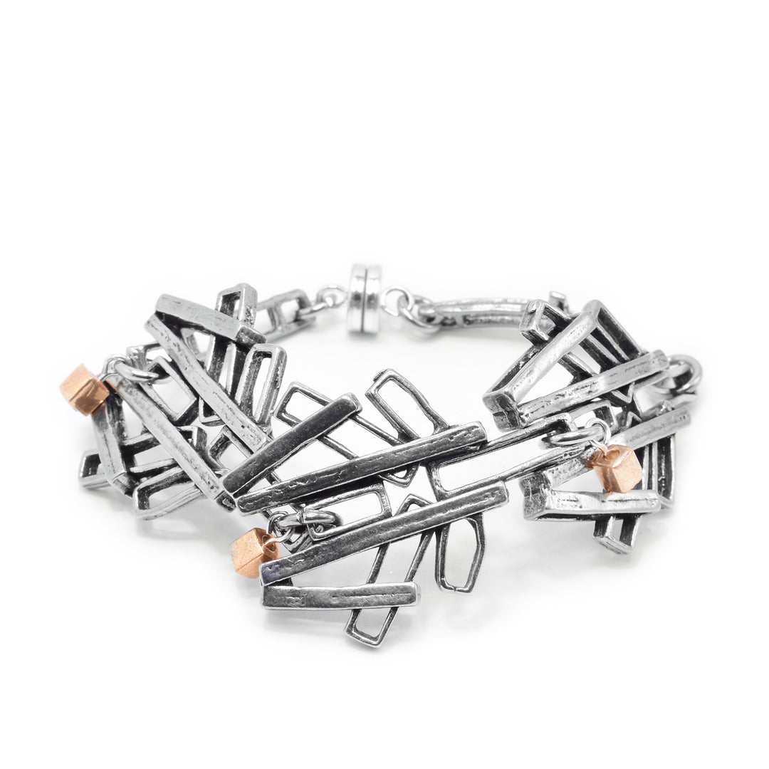 This chunky chain bracelet has large links made from pewter. Each of the links has cutout pieces with some sticking out to the sides and on top of those pieces are strips that branch over them. There are three gold plated cube charms (one on each ink). 