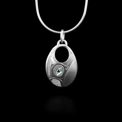 This Hummingbird pendant is wide, oval shaped and has a circle cutout on the top of the pendant. The Hummingbird legend is depicted in side profile and its head is looking upwards. In the spaces behind the legend, there are hatching patterns. There is a blue topaz gems imbedded in the eye of the Hummingbird.