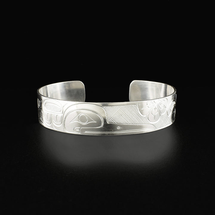 Detailed cuff bracelet depicting a hummingbird in a floral setting. Side-view of the hummingbird’s face is in the center. Design is made from cross-hatching, ovoids and lines.