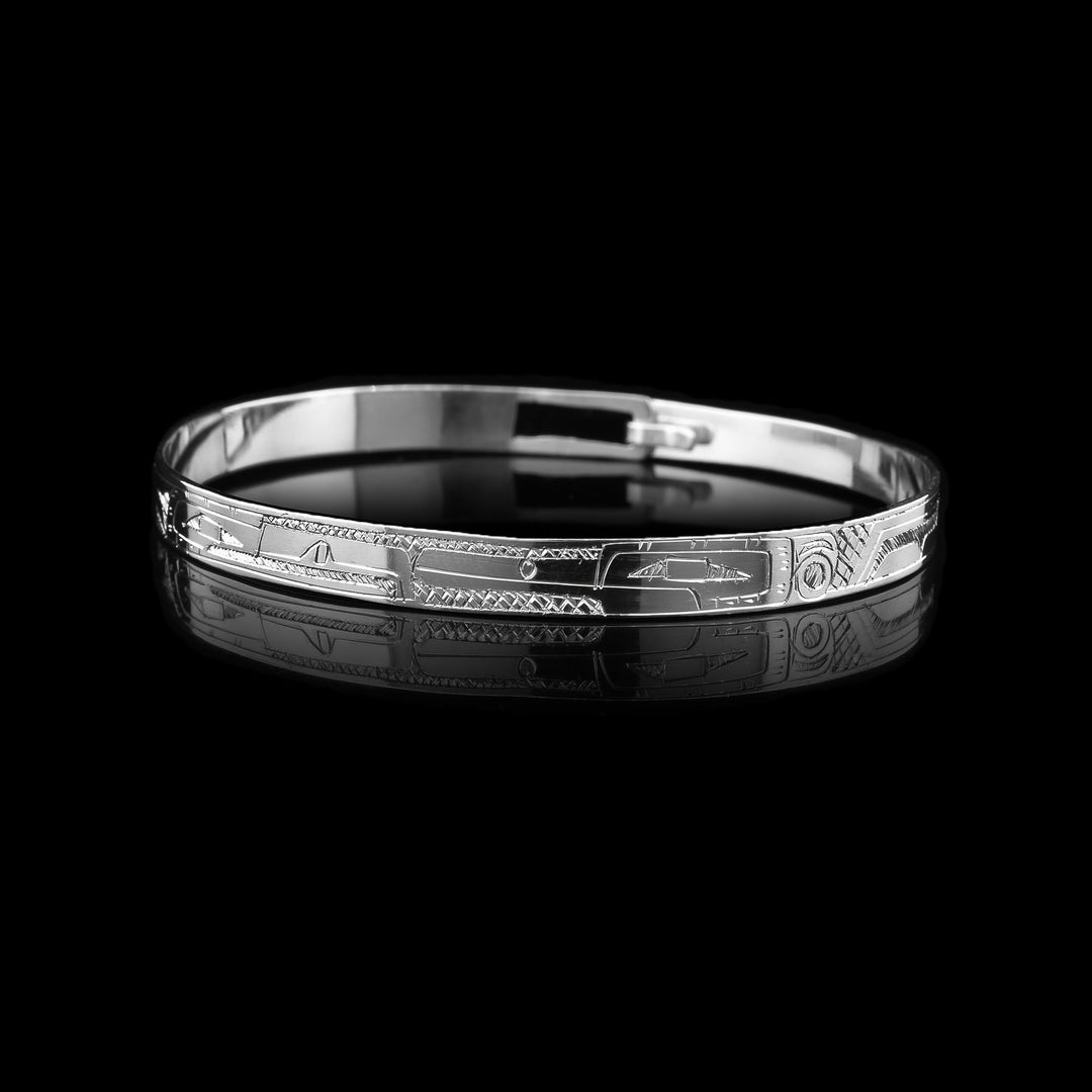 This delicate bangle bracelet features a single, thin band crafted from sterling silver and secured with a clasp at the back. Intricately carved along the band are full-body side profiles of the Eagle and Hummingbird, their faces meeting at the top of the piece in a symbolic and harmonious design.