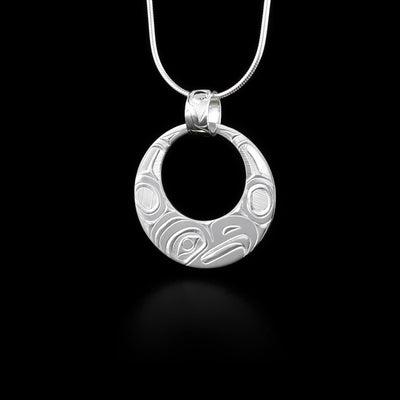 This Eagle pendant is made from sterling silver and has a circle shape with a large, circle shaped cutout in the top. The head of the Eagle is depicted at the side view and its at the bottom of the pendant. There are wing designs extending up on either side carved into the pendant. The pendant hangs from a decorated, wide bail that has designs carved into it.