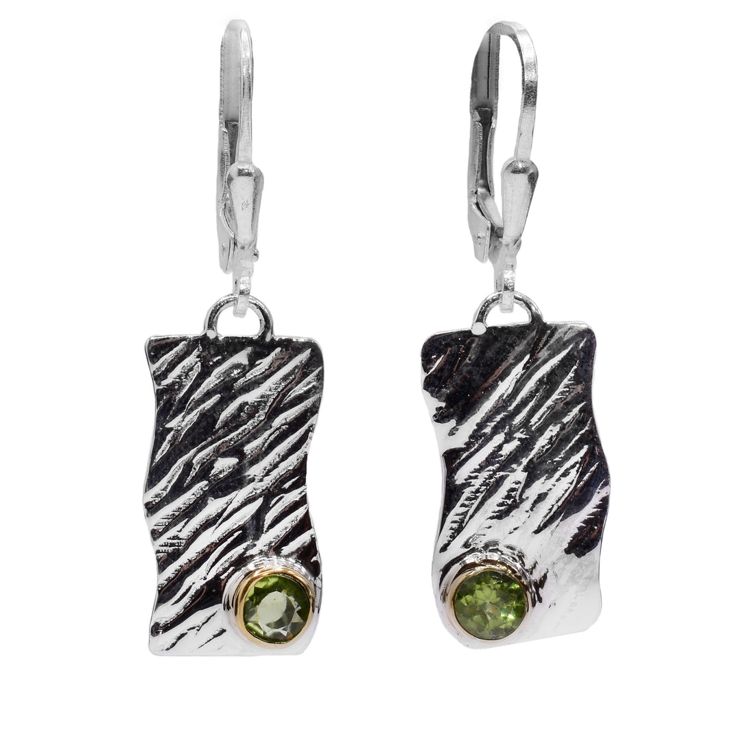 These dangling peridot earrings are made from sterling silver, brass and peridot gems. The hangs are wavy, rectangular and have a rippled textures on the surface of them. There is a circle peridot gem placed in the corner and is held in gold.