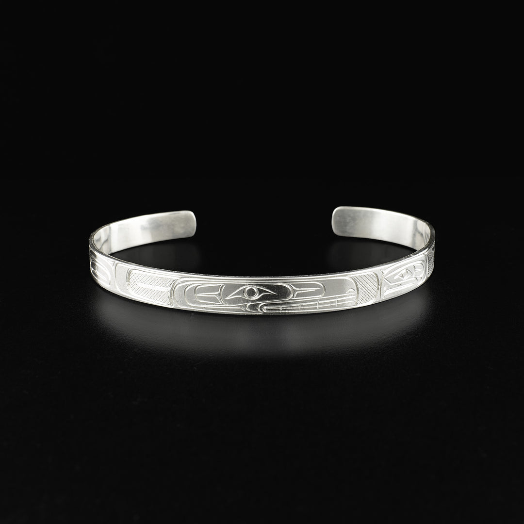 Detailed cuff bracelet depicting an orca and a salmon facing each other. Side view of the orca’s face is in the center. Design is made from cross-hatching, ovoids and lines.