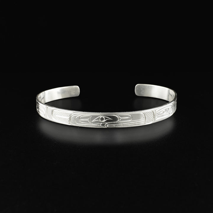 Detailed cuff bracelet depicting an orca and a salmon facing each other. Side view of the orca’s face is in the center. Design is made from cross-hatching, ovoids and lines.