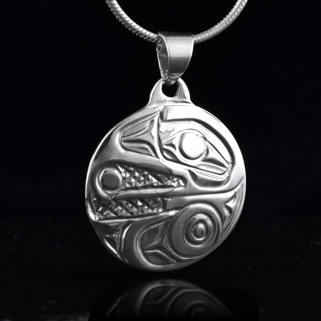 This Raven pendant is made from sterling silver and is circle shaped. The piece shows the face of the Raven  facing sideways, sharp beak detailed holding a pearl inside. 