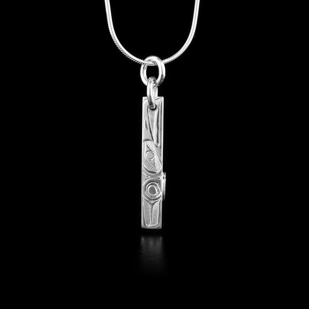 This Raven pendant is sterling silver and has a very thin, rectangle shape. There is a raven depicted in a side view  with its head at the top facing upwards. There is a wing detail carved behind it. On the side of the piece, there is a circle feature midway down it.