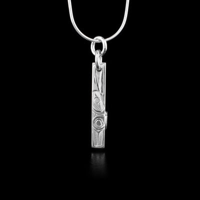 This Raven pendant is sterling silver and has a very thin, rectangle shape. There is a raven depicted in a side view  with its head at the top facing upwards. There is a wing detail carved behind it. On the side of the piece, there is a circle feature midway down it.