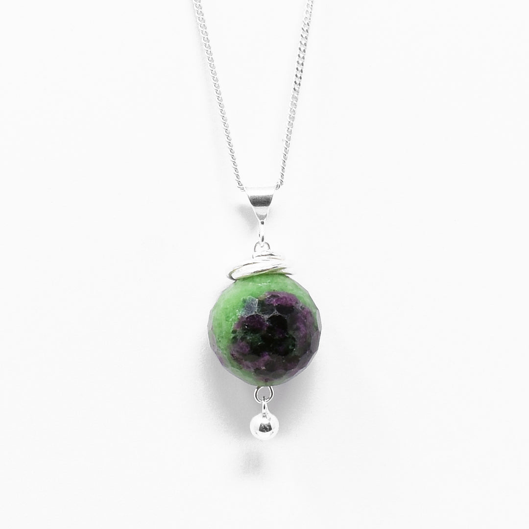 Mulit gemstone pendant. Round, faceted ruby in zoisite with interlocking hoops adornments above and small, round ball of silver dangling below. All metal is sterling silver.