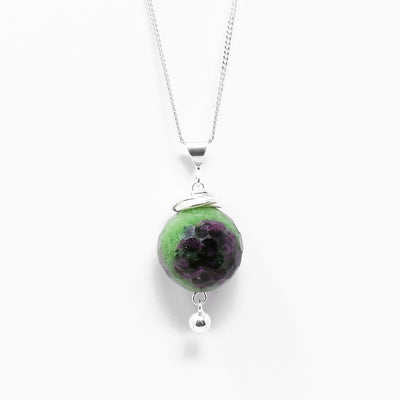 Round, faceted ruby in zoisite with interlocking hoops adornments above and small, round ball of silver dangling below. All metal is sterling silver.