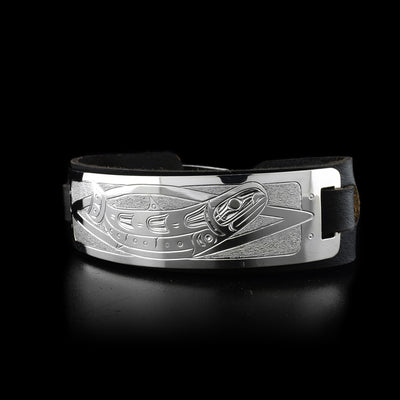 Leather cuff has sterling silver plate with side-view of swimming salmon. Design is done in ovoids, lines and texture. Leather is black.
