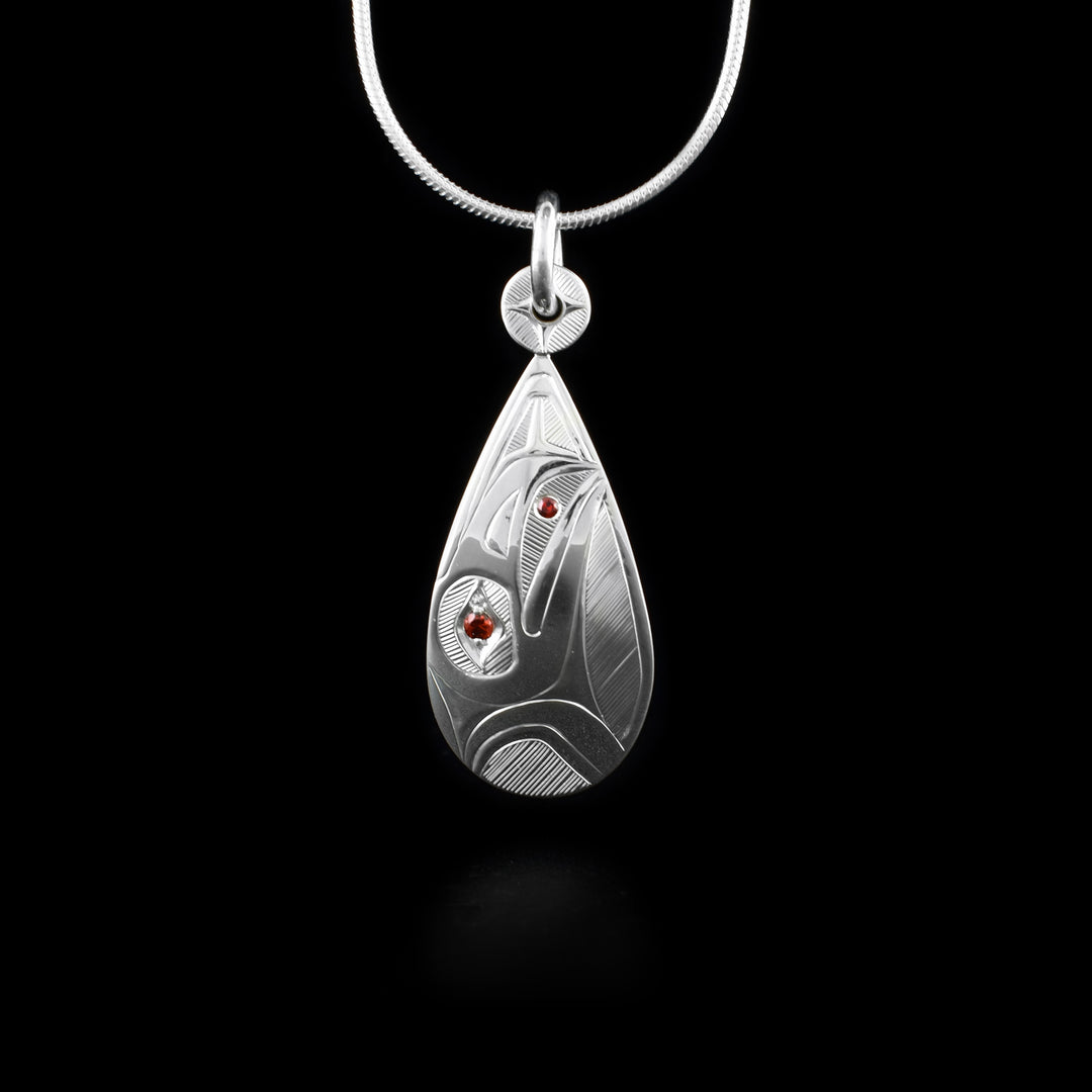 This sterling silver Raven pendant is teardrop shaped and depicts the head of the Raven in a side profile. The head is looking straight up and there is a circle charm on the jump ring. There is a garnet gem in the eye of the Raven and a smaller one held between its beak.