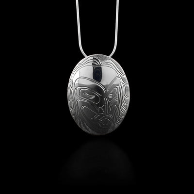 Domed oval pendant. Design depicts woman’s head, showing face and hair. Design is done in ovoids and lines. Textured background. Hidden bail on back.