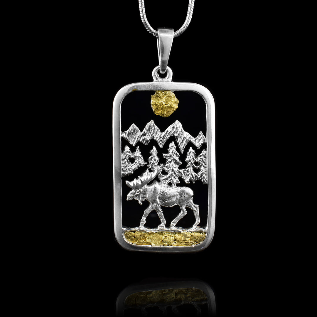 Sterling Silver and 22k Gold Nugget Canadian Landscape Pendant, the pendant feature and moose wandering trough a forest with mountains in the background.