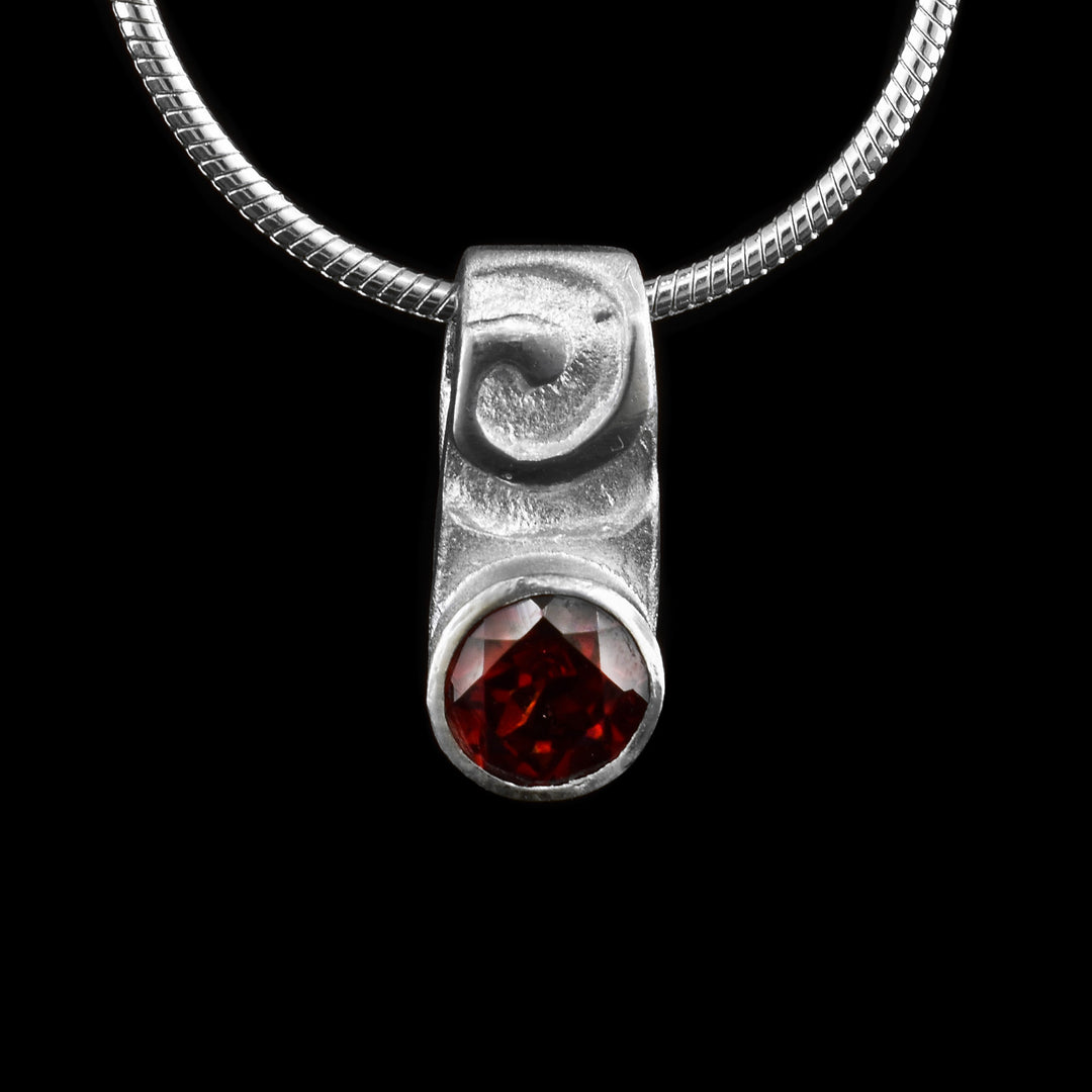 This elegant sterling silver pendant features a delicate swirl design at the top and below is a red garnet.