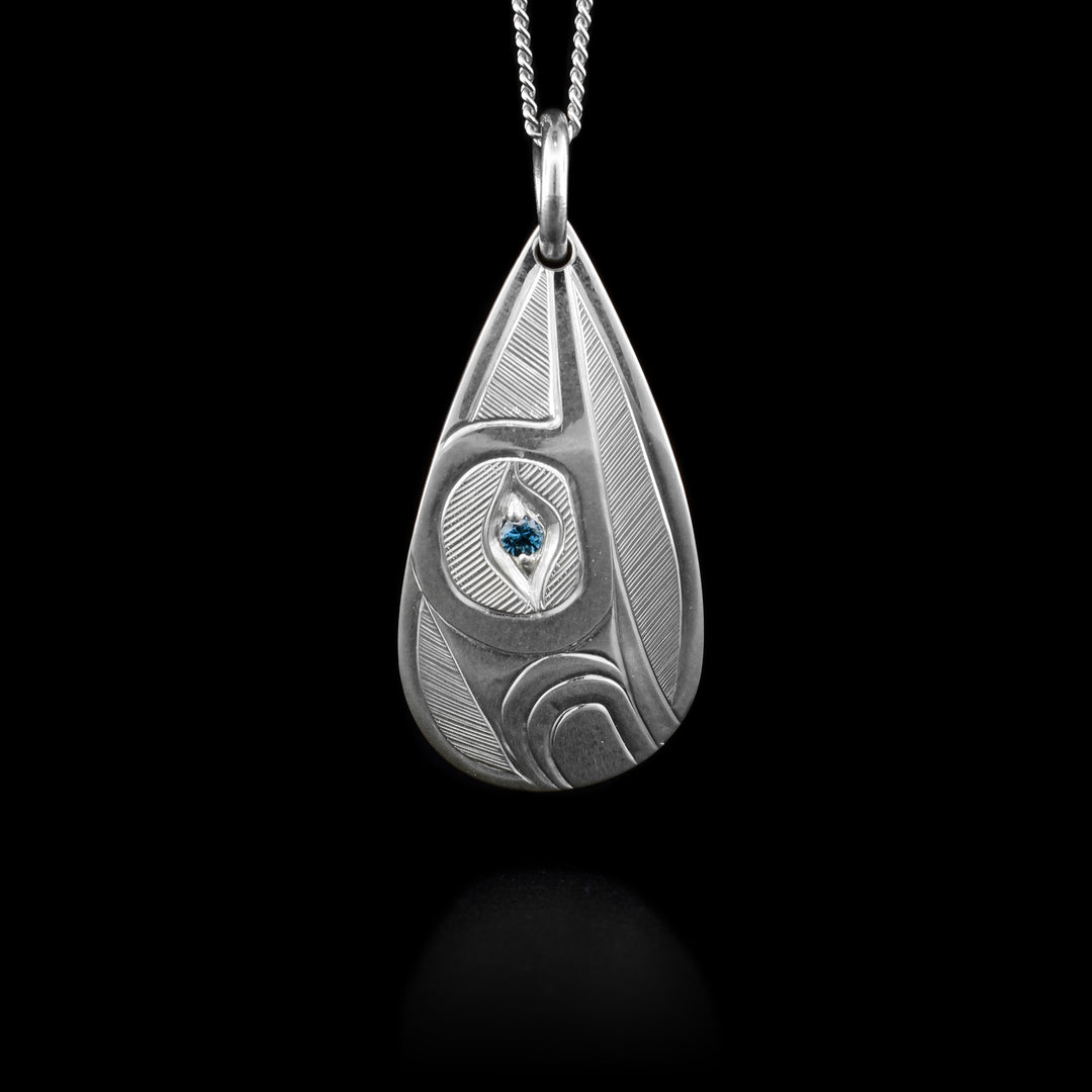 This Hummingbird pendant has a side-view of top half of hummingbird facing upwards with a blue topaz set in eye. Hand-carved by Haisla artist Hollie Bartlett.