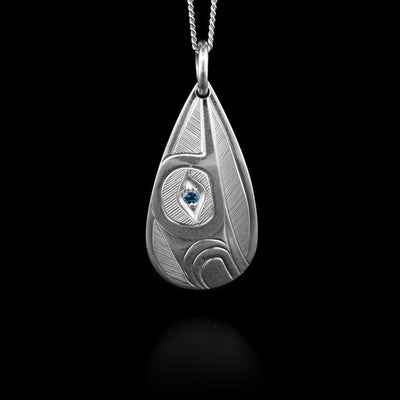 Side-view of top half of hummingbird facing upwards with a blue topaz set in eye. Hand-carved by Haisla artist Hollie Bartlett.