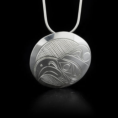 This Thunderbird pendant is circular in shape and depicts the head of a thunderbird facing the right when worn. The background has been cross-hatched.