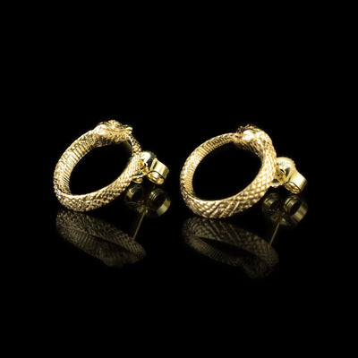 These ouroboros earrings are made from 10K gold and are circle shaped. The studs are attached to the tops of the circles and they look like snakes with their tails curled up into their mouths. There are scale details on the studs and they have detail heads.