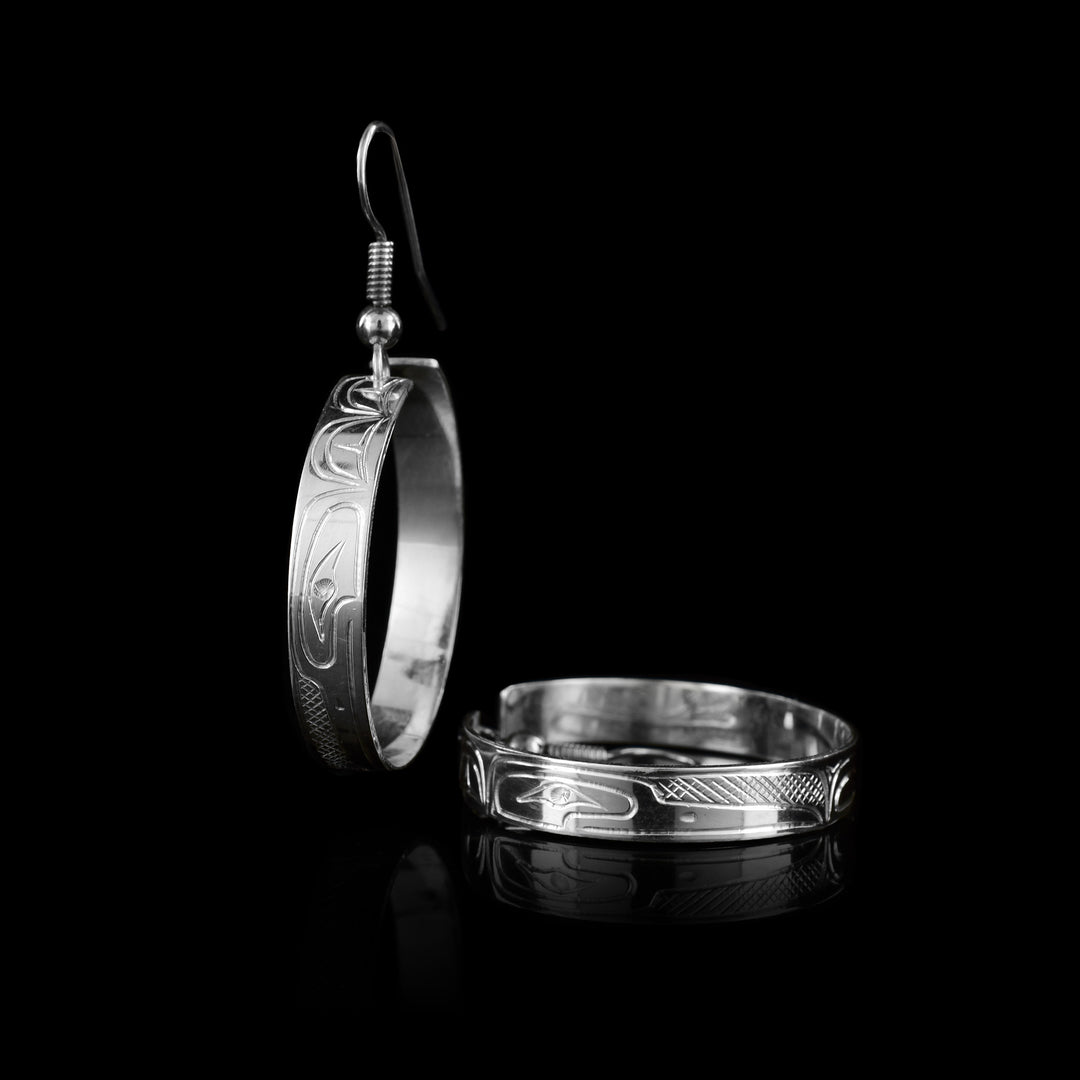 Handcrafted by Coast Salish artist Travis Henry, these sterling silver 1 inch wide dangle hoop earrings feature a beautifully carved Hummingbird legend.